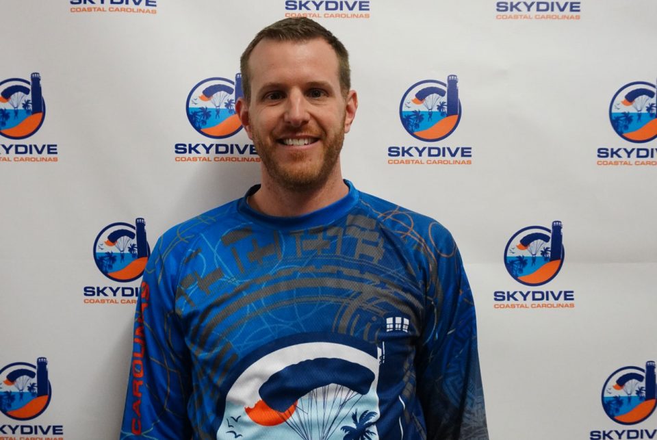 Headshot of Skydive Coastal Carolinas skydiving instructor and co-owner Blake Strong in front of backdrop with Skydive Coastal Carolinas logo