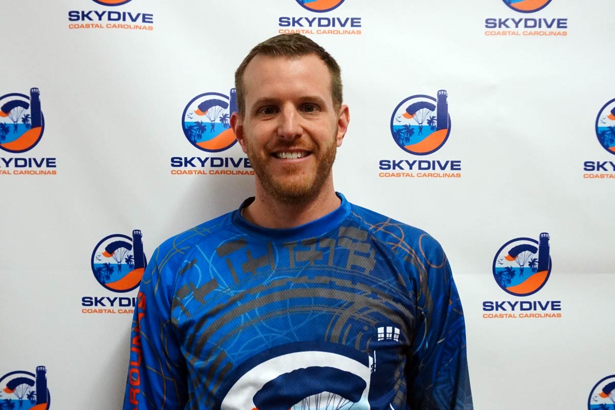 Headshot of Skydive Coastal Carolinas skydiving instructor and co-owner Blake Strong in front of backdrop with Skydive Coastal Carolinas logo