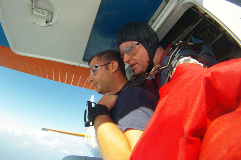 Male tandem skydiving student and male tandem instructor kneel and prepare to exit the aircraft