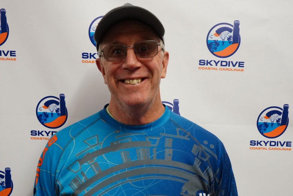 Headshot of Skydive Coastal Carolinas owner Brian Strong in front of backdrop with Skydive Coastal Carolinas logo