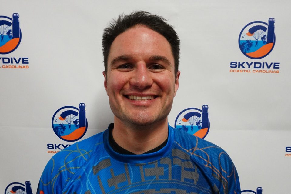 Headshot of of Skydive Coastal Carolinas skydiving instructor Christopher Dunbar in front of backdrop with Skydive Coastal Carolina Logo