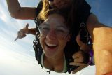 Grinning tandem skydiving student with nose ring makes shaka gesture with both hands in freefall