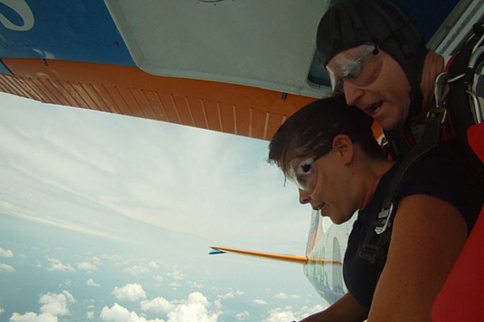 Female tandem student and male tandem skydiving instructor prepare to exit the Cessna-182 with puffy white clouds waiting below