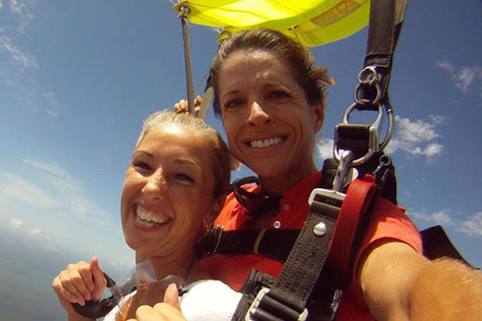 Smiling faces of female tandem instructor and female tandem skydiving student while flying under canopy