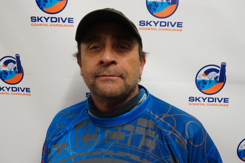 Headshot of of Skydive Coastal Carolinas skydiving instructor Michael Daniel in front of backdrop with Skydive Coastal Carolina Logo