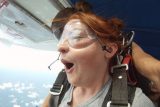 Adorable tandem skydiving student with red hair and freckles gapes open mouthed just before exit