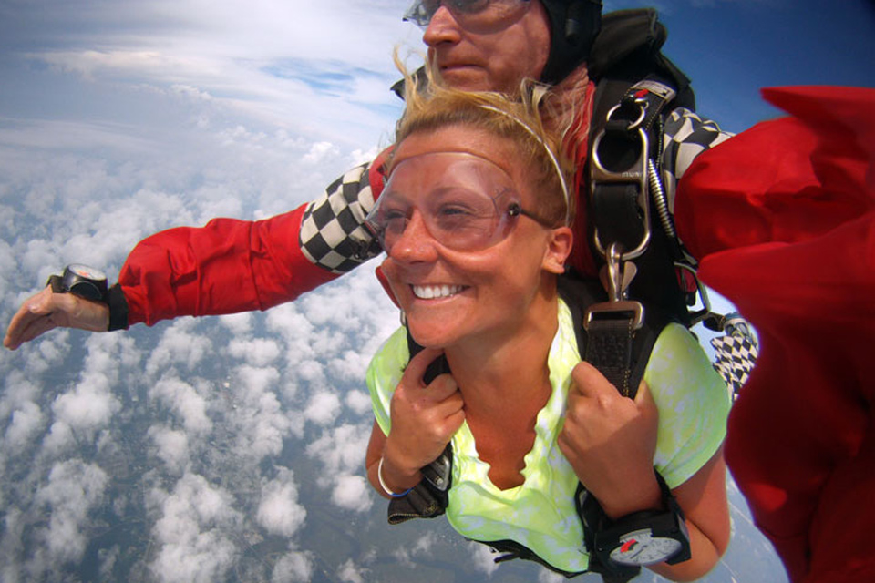 Smiling tandem student grips tandem skydiving harness during freefall