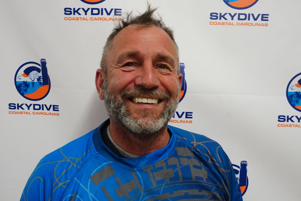 Headshot of Skydive Coastal Carolinas skydiving instructor Thomas Herzog in front of backdrop with Skydive Coastal Carolinas Logo