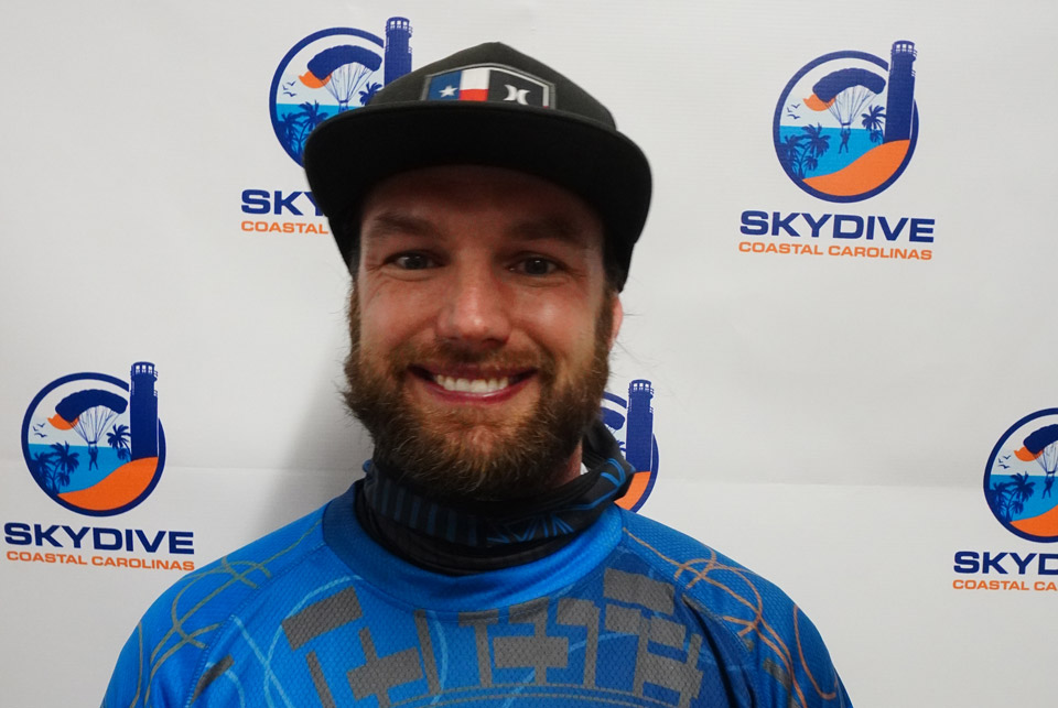 Headshot of of Skydive Coastal Carolinas skydiving instructor Tyler Clark in front of backdrop with Skydive Coastal Carolinas logo