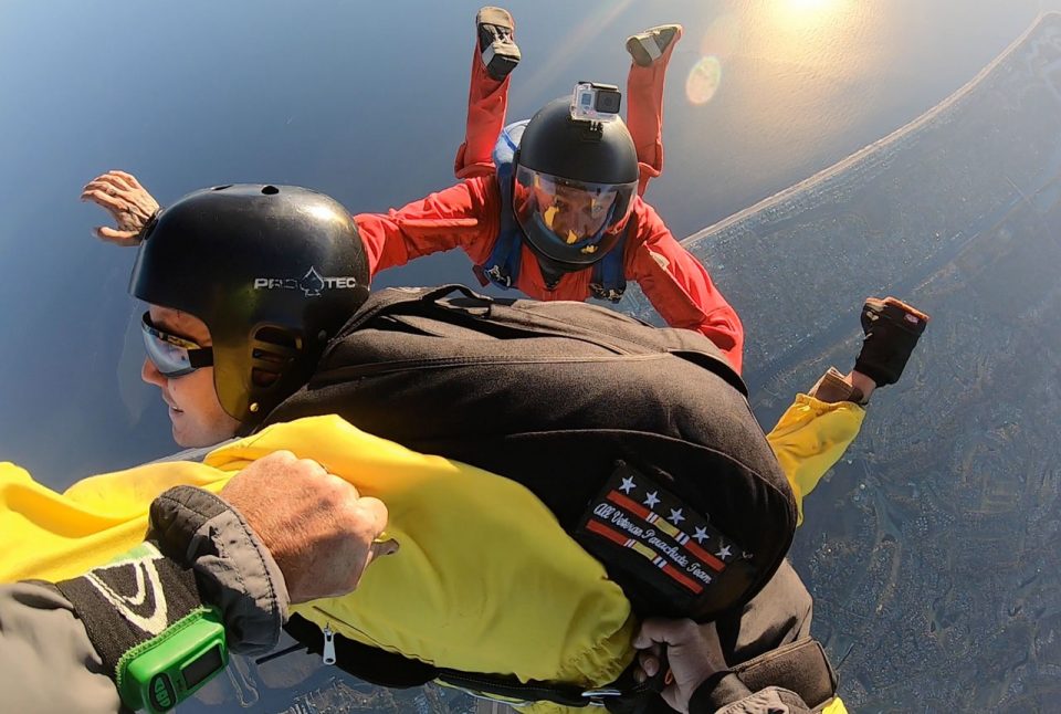 Accelerated Freefall instructor in a red relative work suit on main side looking over accelerated freefall student in a yellow jumpsuit to the reserve side instructor