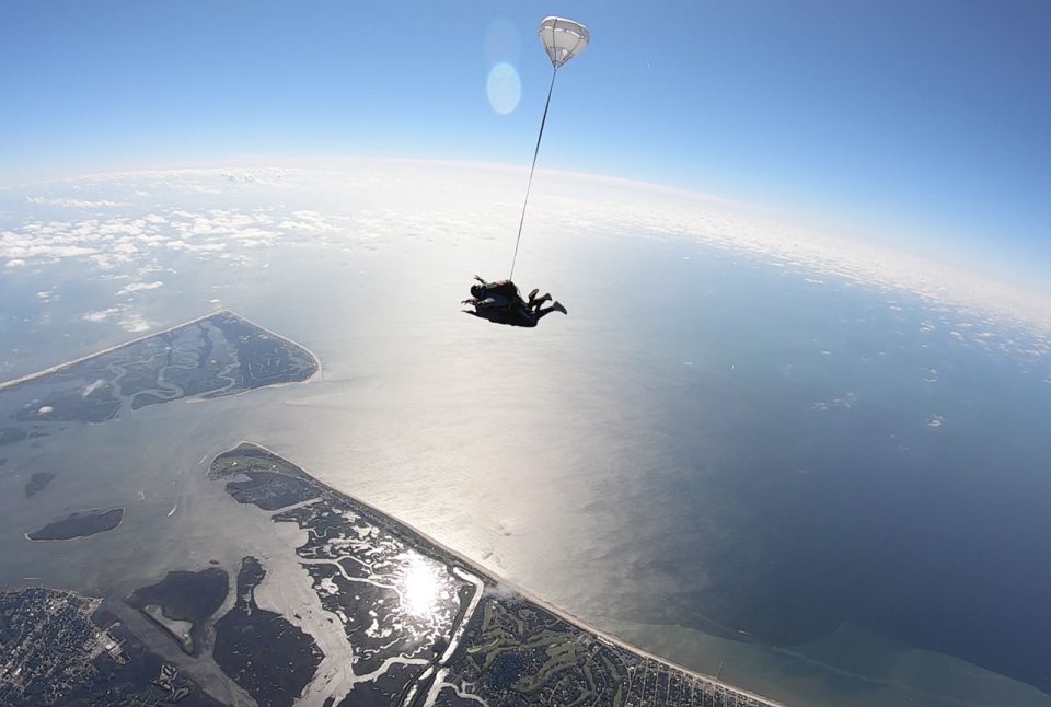 Silhouette of tandem skydiving pair in freefall skydiving on the beach