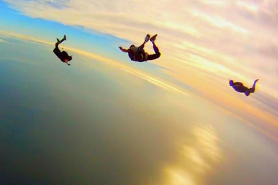 Silhouettes of three skydivers in freefall backlit by sunset