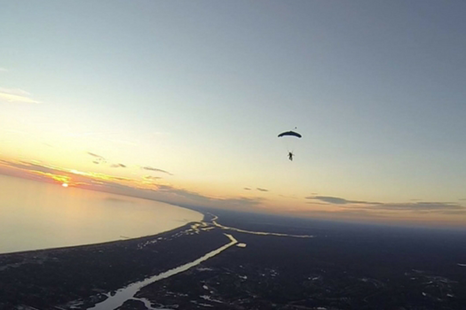 Out of focus licensed skydiver flying over coast at sunset
