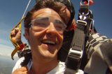 Elated tandem skydiving student enjoys the ride beneath the parachute
