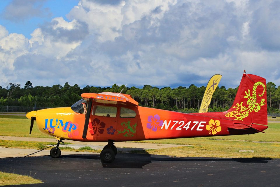 Tropically painted orange Cessna- 182 with multicolored hibiscus flowers, bright green frog, and a tribal gecko design on the tail