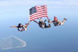 Three licensed skydivers holding the American flag in freefall over the ocean