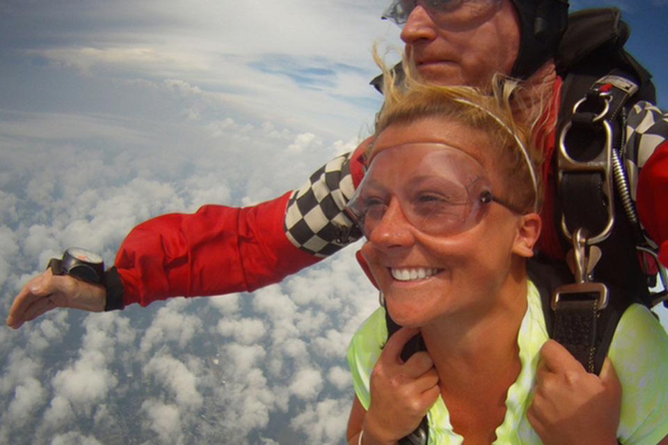 Smiling tandem student grips tandem skydiving harness during freefall