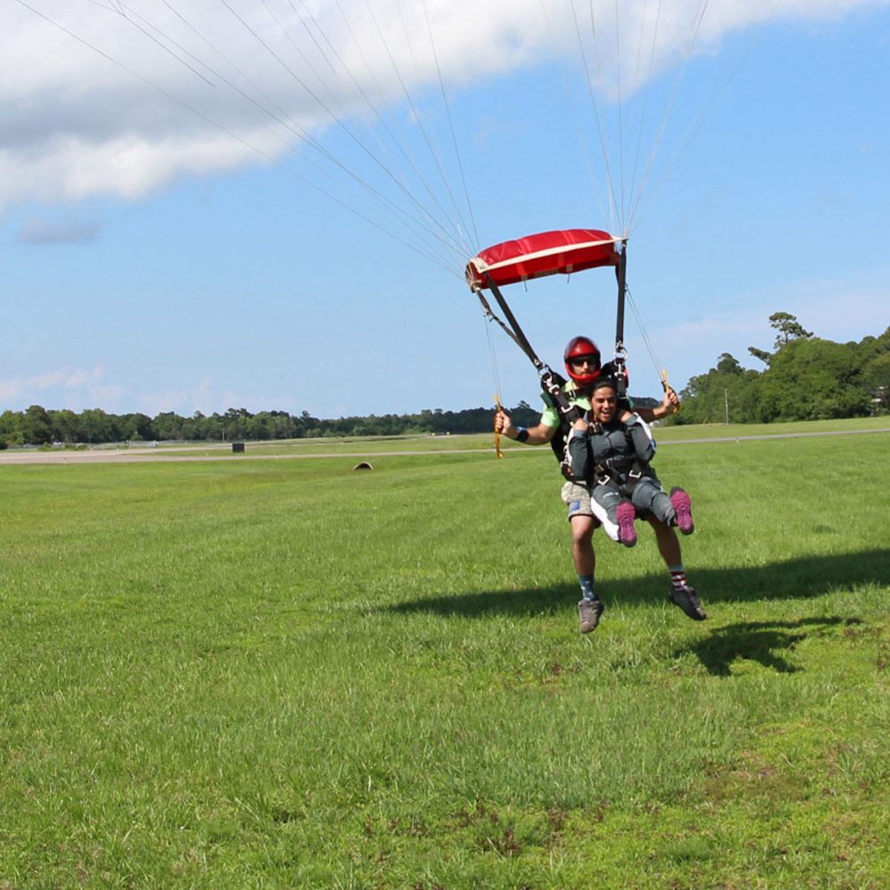 Tandem instructor and excited student land the parachute gently on bright green grass in Oak Island, NC