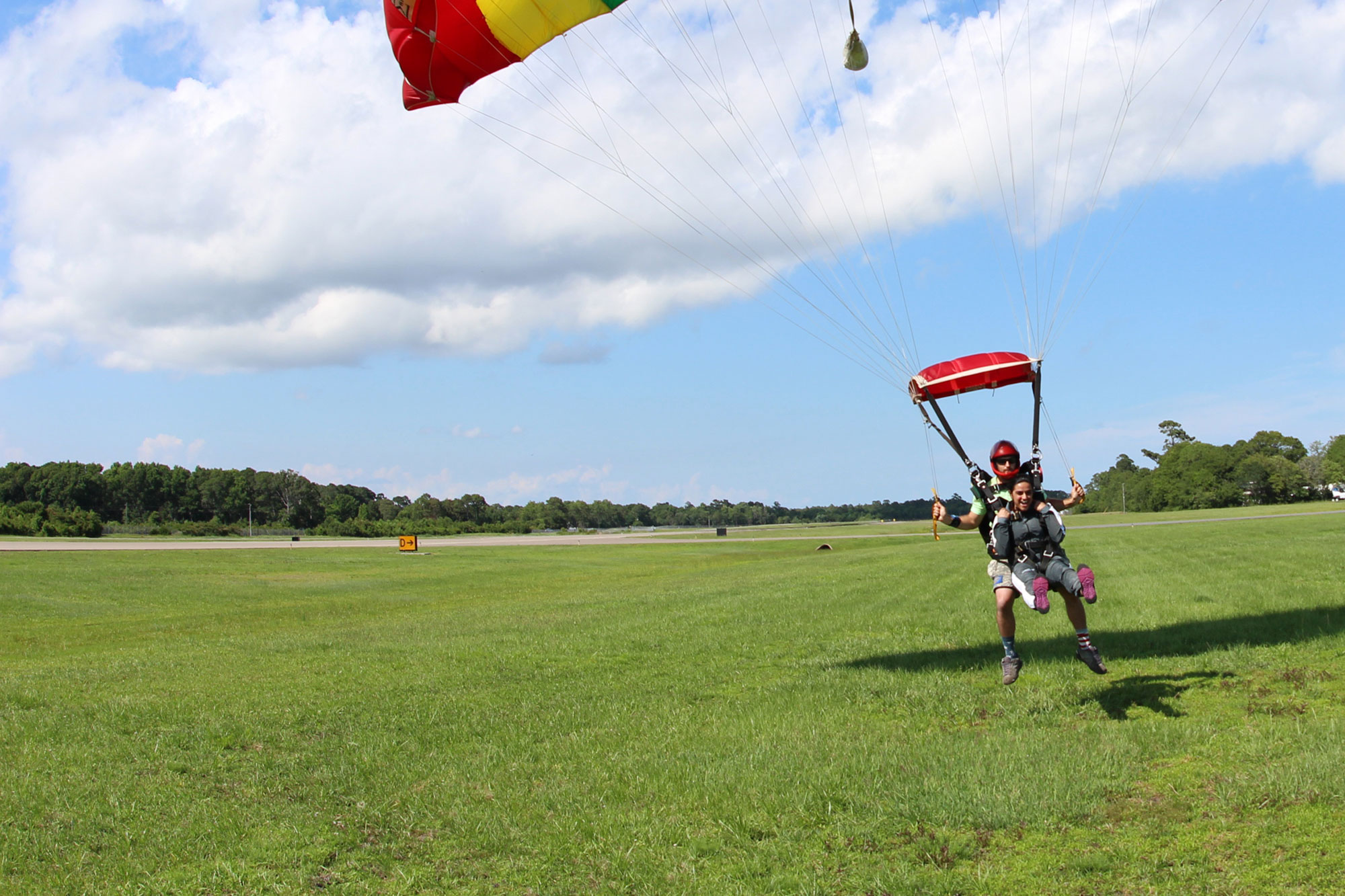 Tandem skydiving student grips harness and raises legs 90 degrees to prepare for landing as the instructor behind her flares the parachute