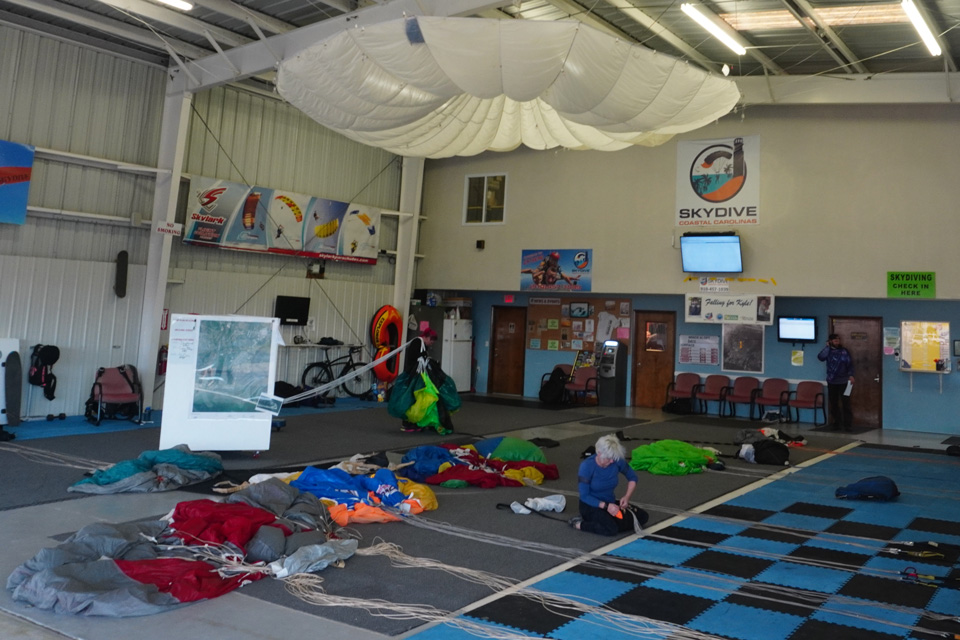 Female in blue shirt packing parachute in the hangar on a packing mat littered with brightly colored canopies