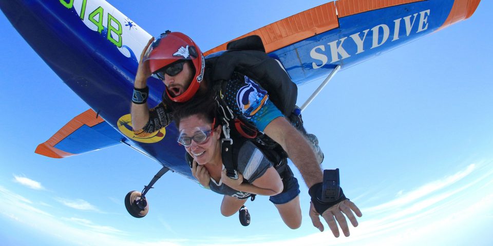 Tandem skydiving student and instructor exiting Cessna-182 painted with blue waves near Myrtle Beach