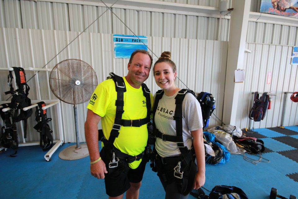 Two first time tandem skydiving students in harnesses smiling for a photo before preparing to skydive near Myrtle Beach