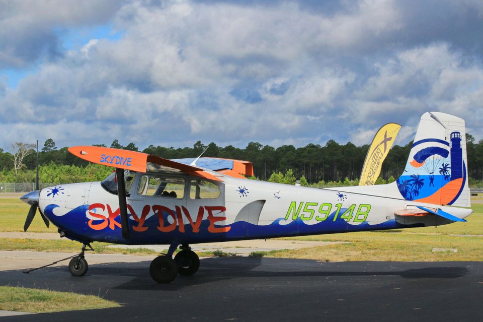 Side view of custom painted Cessna 182 aircraft with blue waives, a shark fin, and the Skydive Coastal Carolinas logo painted on the tail