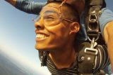 Tan skinned tandem skydiving student in freefall looks to the distance with a smile