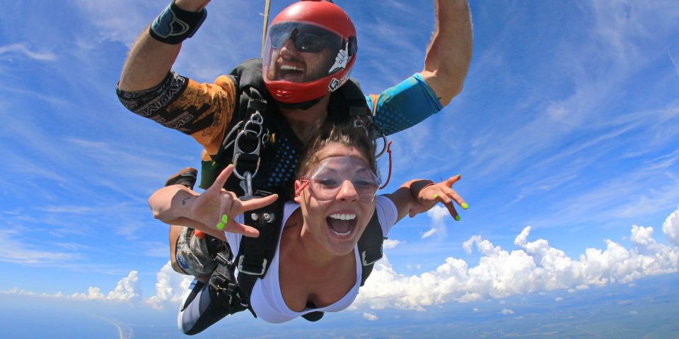 Attentive tandem skydiving instructor checks altitude as tandem skydiving student makes the I love you sign with each hand