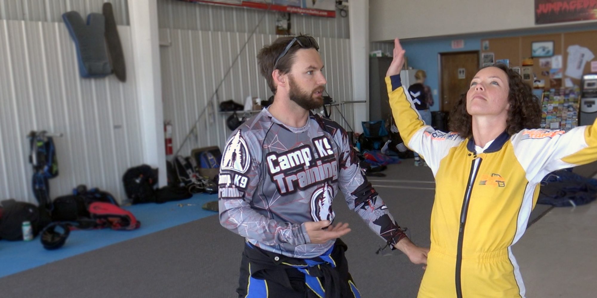 Curly haired female skydiving student in yellow jump suit practices her arch body position as skydiving instructor provides instruction before skydiving in Wilmington, NC