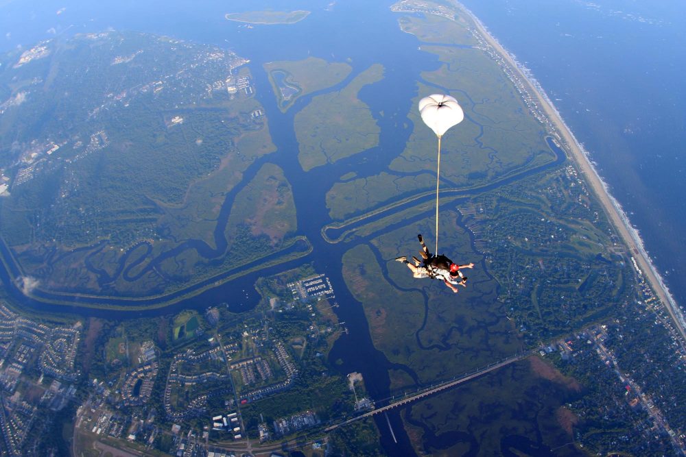 Top view of tandem skydiving pair in freefall with the drogue inflated over the intracoastal waterway of Oak Island, NC