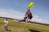 Female tandem skydiving instructor and female student beneath a parachute lift their legs preparing to slide in for landing