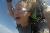 Young female tandem skydiver with hoop nose ring lets out an exhilarated whoop