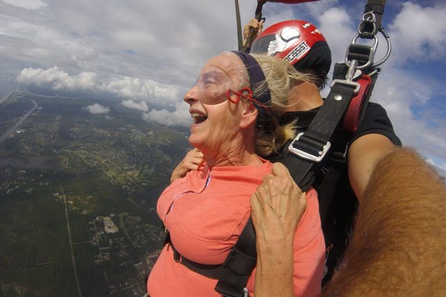 Older female tandem skydiving student with inspired expression takes in the view beneath canopy